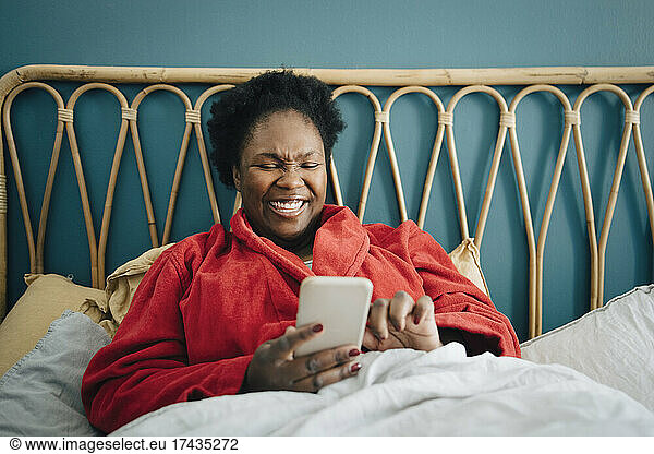 Happy mid adult woman using smart phone on bed at home
