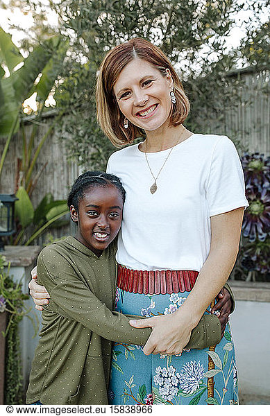 Happy mid-40's white mom hugging 8-yr-old black daughter