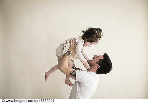Happy Millennial Hipster Father Holds Toddler Girl Above His Head