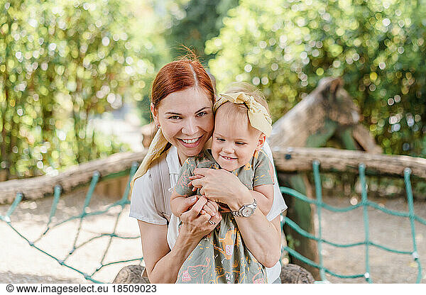 Happy mom and toddler girl hugging and laughing in the playground