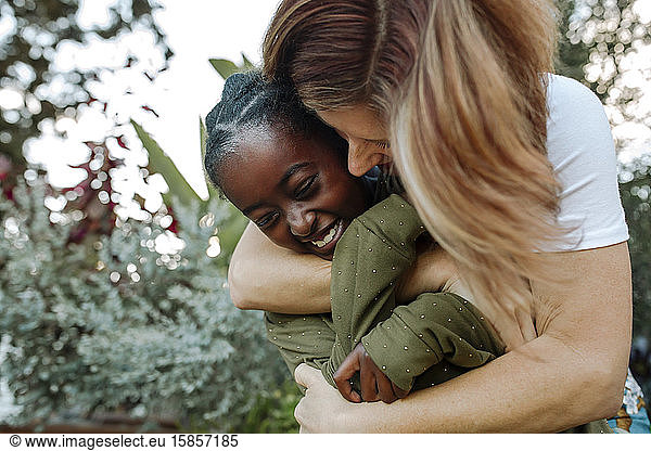 Happy mom hugging smiling daughter with lush green background