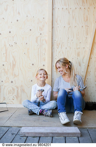 Happy mother and daughter holding hammers against wall of house being renovated