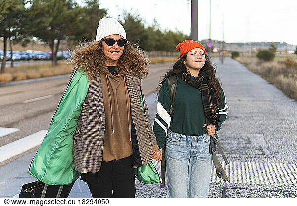 Happy mother and daughter holding hands walking on road