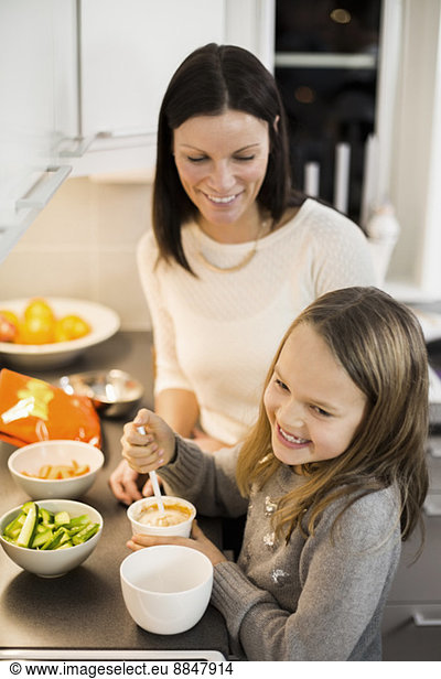 Happy mother and daughter preparing salad in kitchen