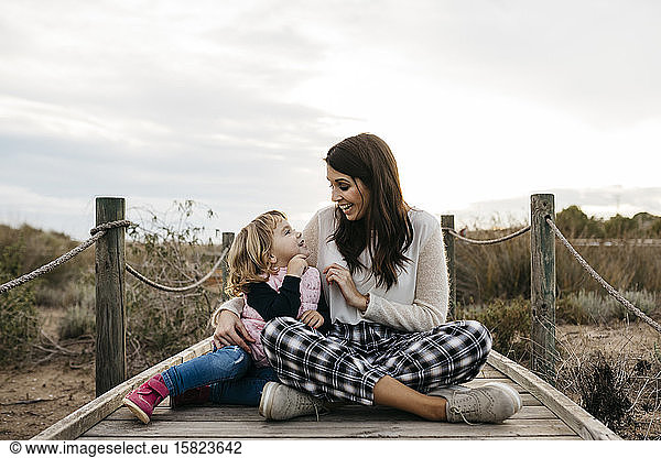 Happy mother and daughter sitting on a boardwalk in the countryside