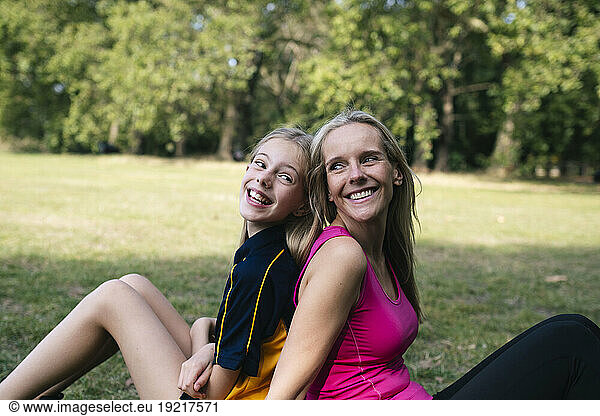 Happy mother and daughter sitting on grass in park