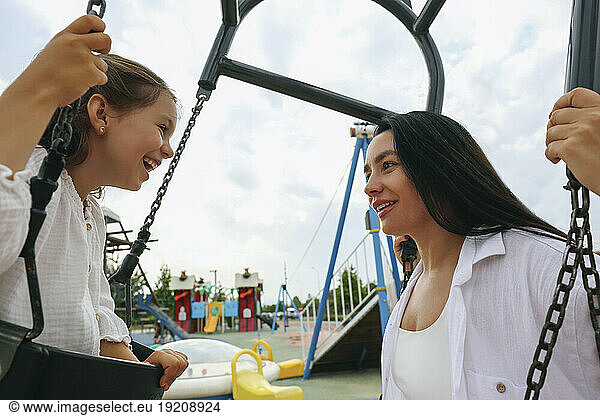 Happy mother and daughter swinging on swing at playground