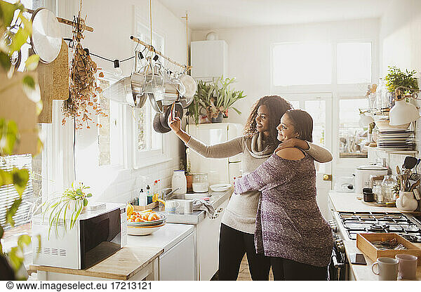 Happy mother and daughter taking selfie in sunny kitchen