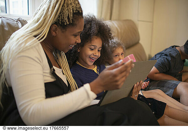 Happy mother and daughter using digital tablet on living room sofa