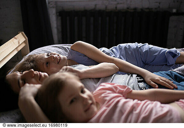 Happy mother and daughters resting on bed