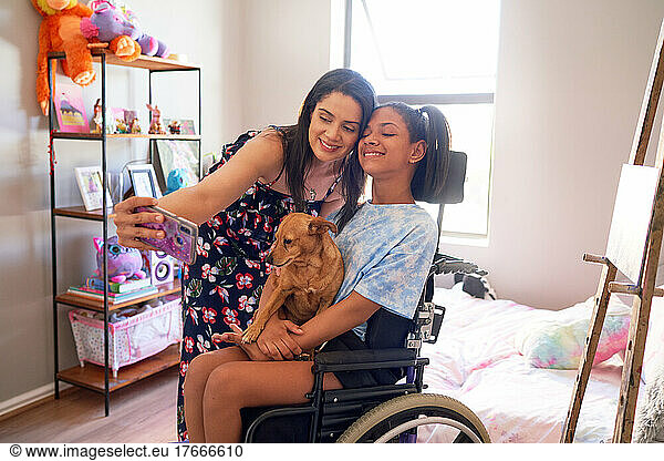 Happy mother and disabled daughter with dog taking selfie at home