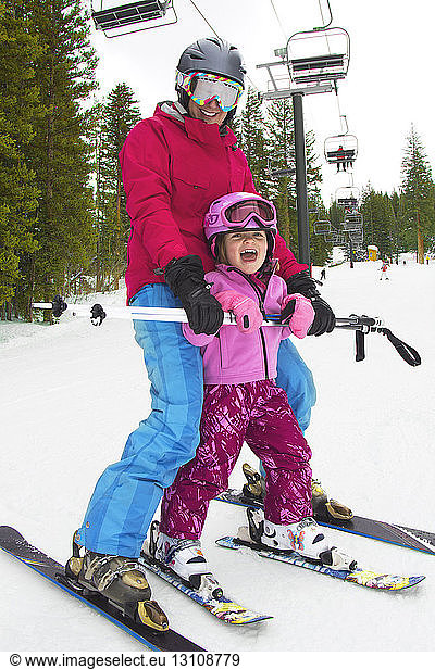 Happy mother and girl skiing on snow covered field