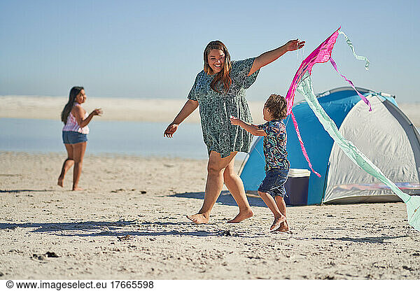 Happy mother and son playing with kite on sunny beach