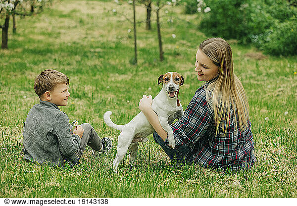 Happy mother and son sitting with Jack Russell Terrier dog in garden
