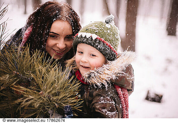 Happy mother and son standing by Christmas tree outdoors in winter