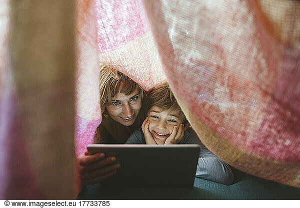 Happy mother and son using tablet PC under blanket