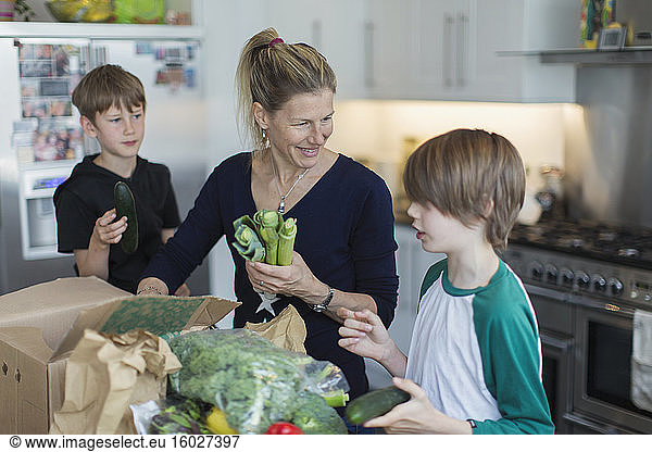 Happy mother and sons unloading fresh produce from box in kitchen