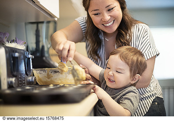 Happy mother and toddler daughter baking muffins in kitchen