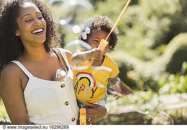 Happy mother and toddler daughter playing with bubble wand in sunshine
