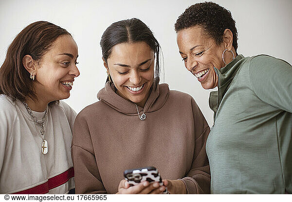 Happy mother and young adult daughters using smart phone