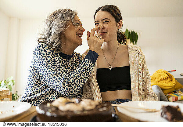 Happy mother applying chocolate on nose of daughter at home