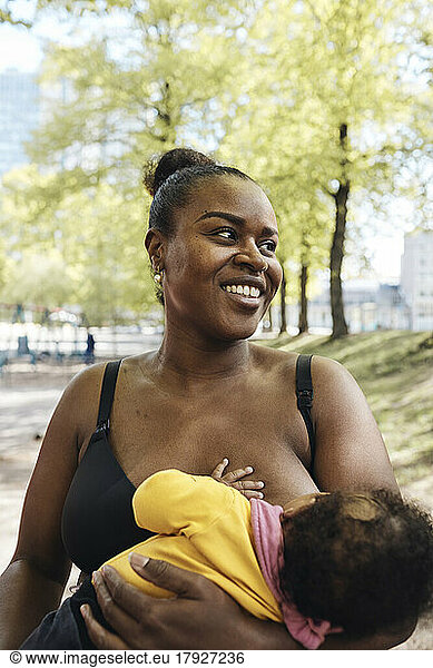 Happy mother breastfeeding daughter at park