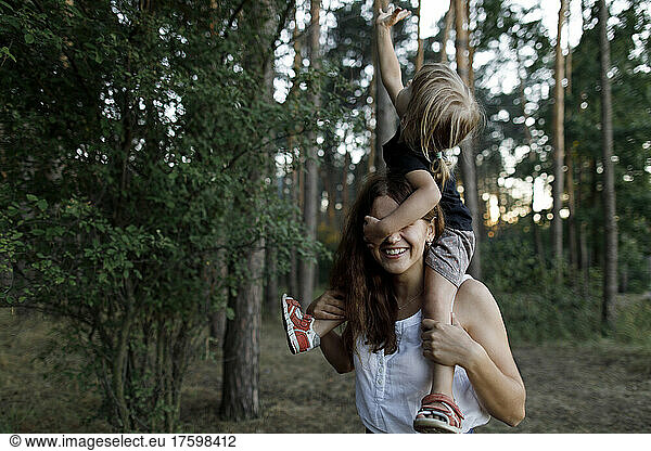 Happy mother carrying daughter on shoulder in forest