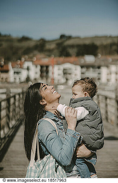 Happy mother carrying son at jetty on sunny day