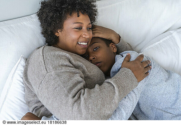 Happy mother cuddling son in bed at home