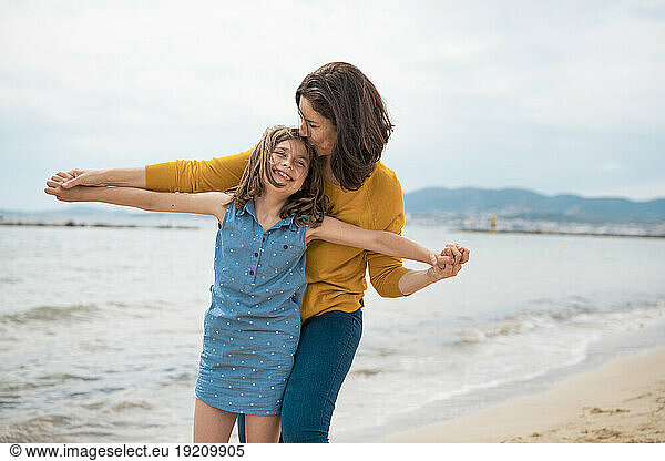 Happy mother embracing and kissing daughter in front of sea at beach