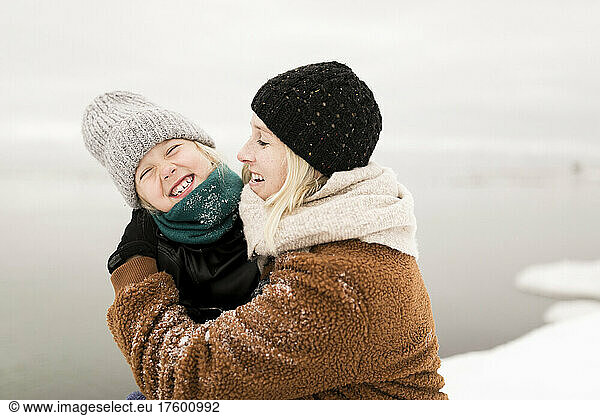 Happy mother embracing cheerful daughter enjoying in winter