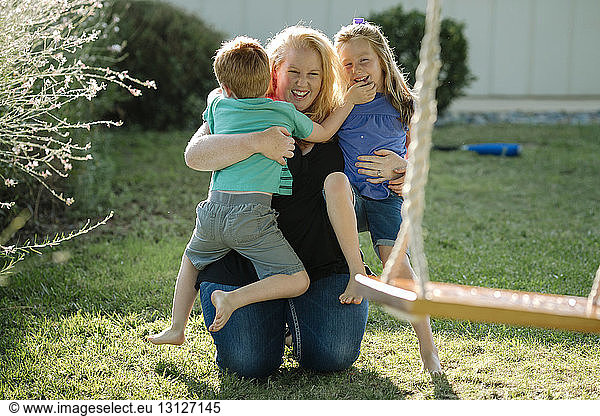 Happy mother embracing children while kneeling at front yard