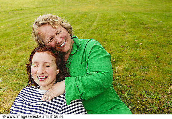 Happy mother embracing daughter sitting on grass