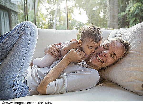 Happy mother having fun with daughter on sofa in living room at home