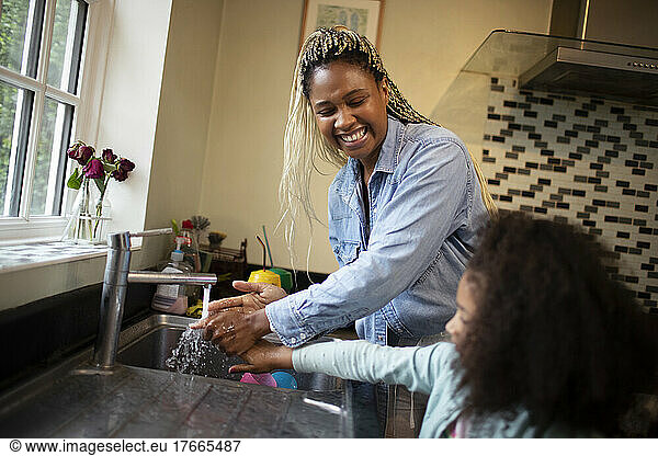 Happy mother helping daughter wash hands at kitchen sink