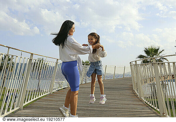 Happy mother holding hands with daughter jumping on bridge