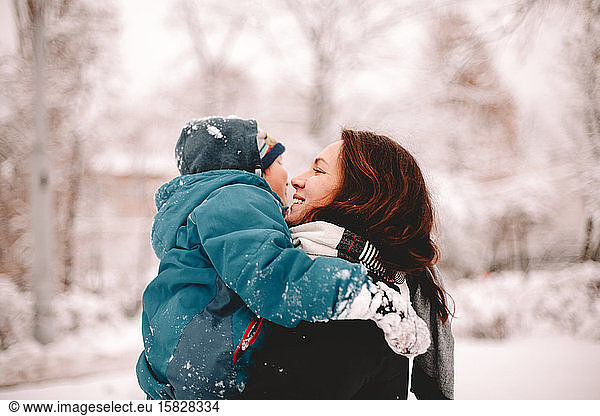 Happy mother holding son while standing in park during winter