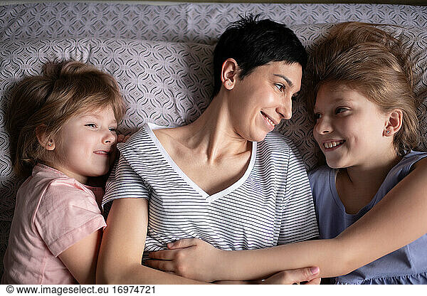 Happy mother hugging daughters in bed in morning