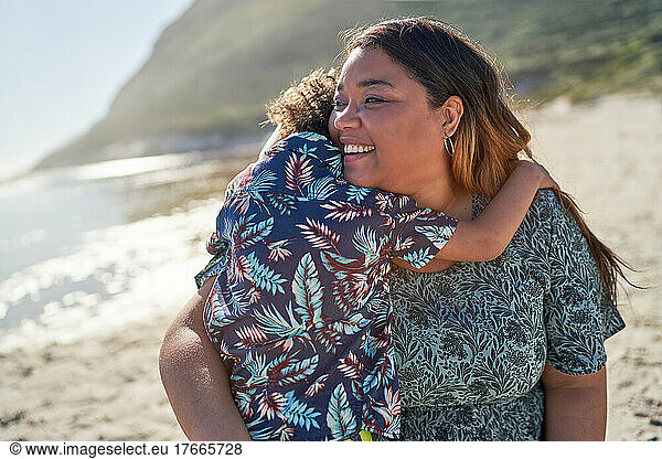 Happy mother hugging son on sunny beach