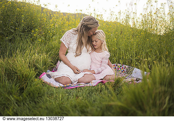 Happy mother kissing daughter on forehead while sitting in park