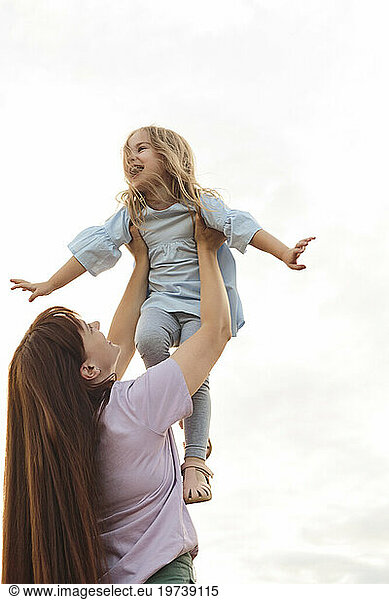 Happy mother lifting daughter under sky