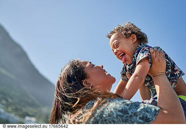 Happy mother lifting son with Down Syndrome below sunny blue sky