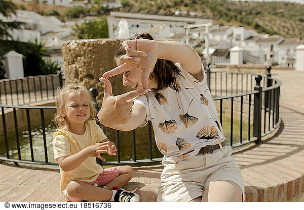 Happy mother making finger frame with daughter on sunny day