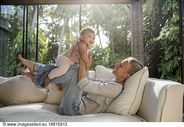 Happy mother playing with daughter on sofa in living room