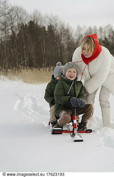Happy mother pushing sons sitting on toboggan in winter