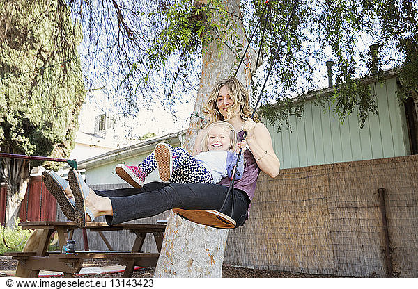 Happy mother swinging with daughter in backyard