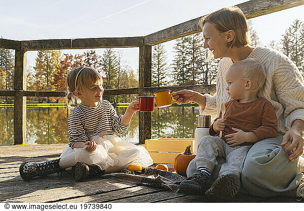 Happy mother toasting hot chocolate cups on footbridge