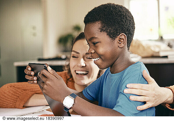 Happy mother with arm around son enjoying while watching digital tablet at home