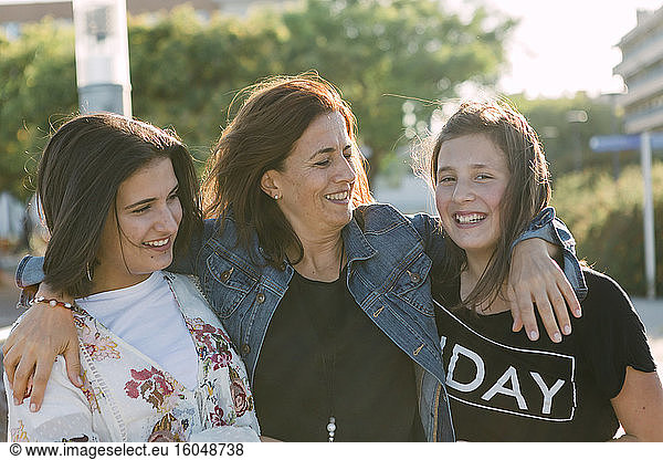 Happy mother with arms on daughters standing outdoors