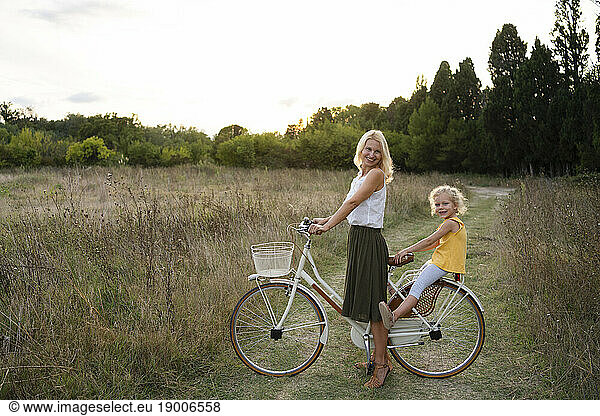 Happy mother with daughter sitting on bicycle at sunset